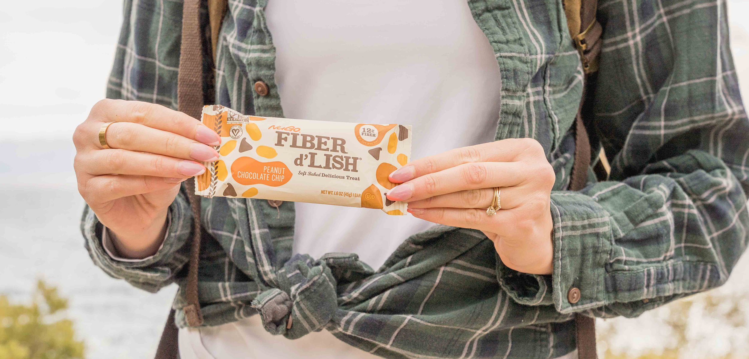 Woman, outisde, hold NuGo Fiber Peanut Chocolate Chip bar in front of body