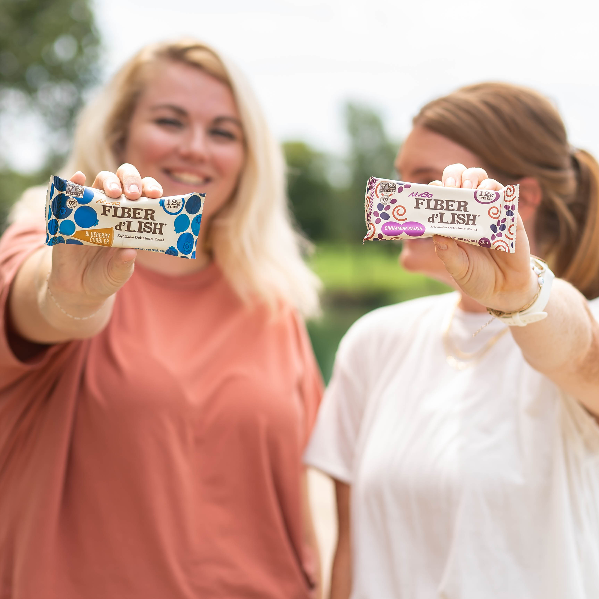 two smiling friends hold NuGo Fiber bars straight out