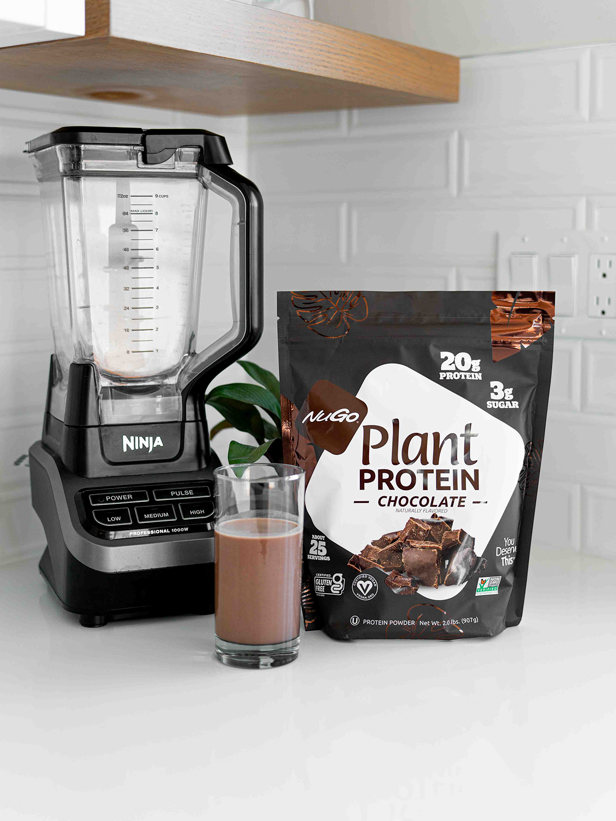 A bag of Chocoalte NuGo Protein Powder next to a blender and glass of it mixed