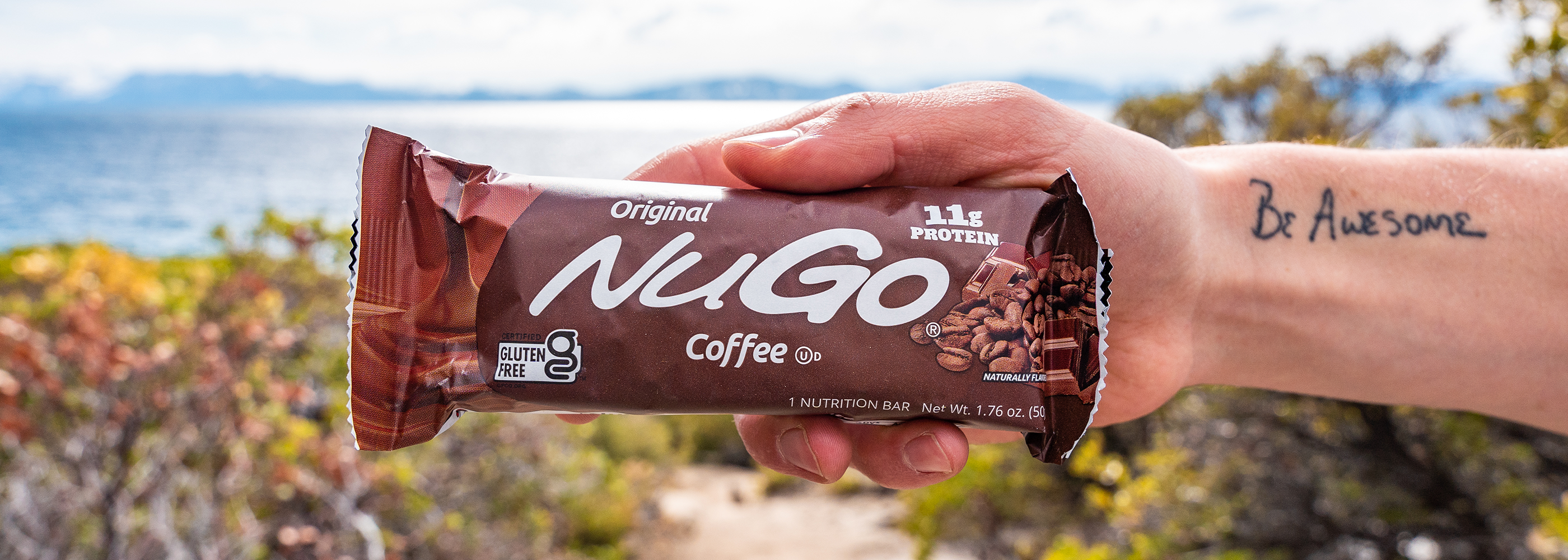 Close up NuGo Original Coffee being held in front of lake and country-scape