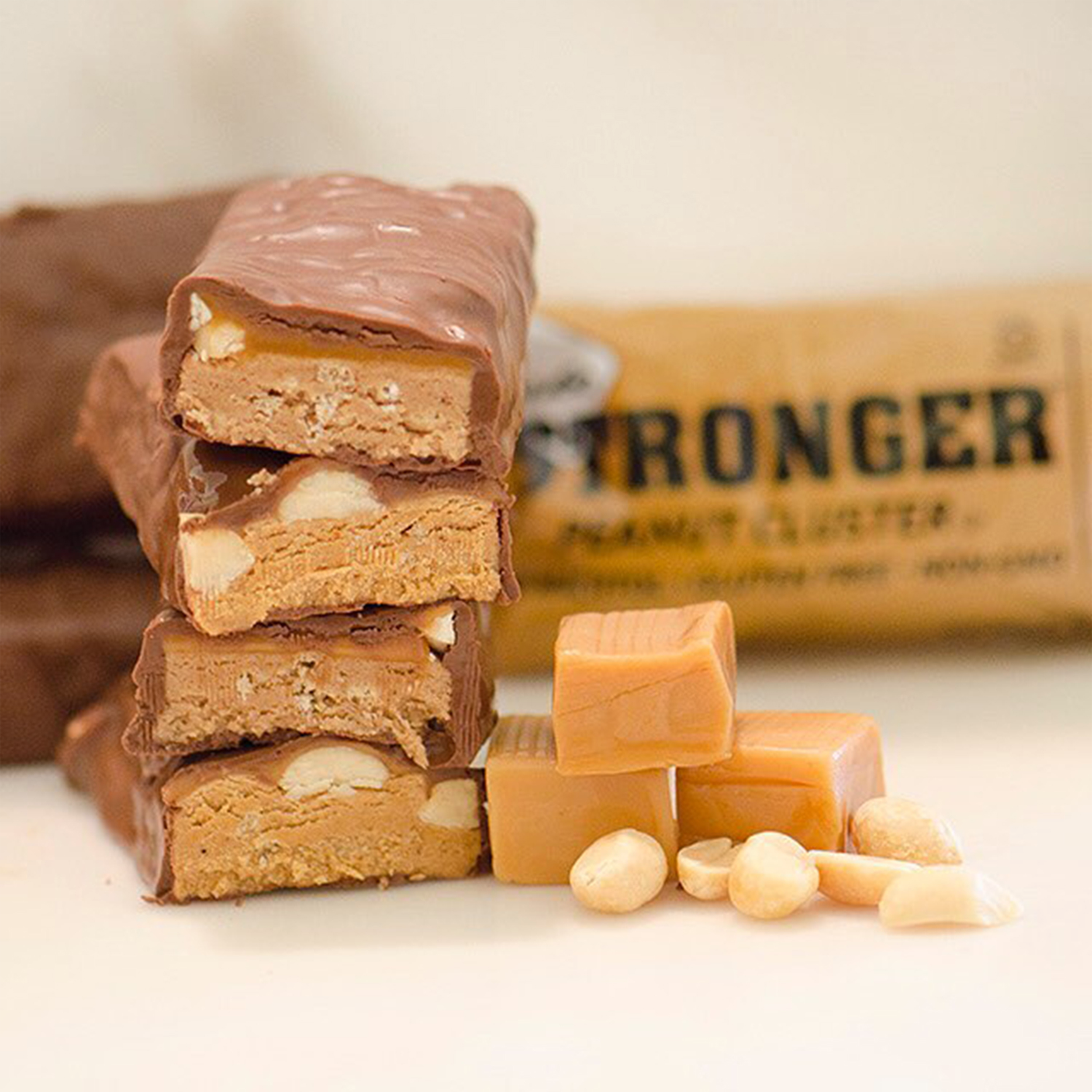 NuGo Stronger Peanut Cluster stacked next to caramel squares in front of wrapper