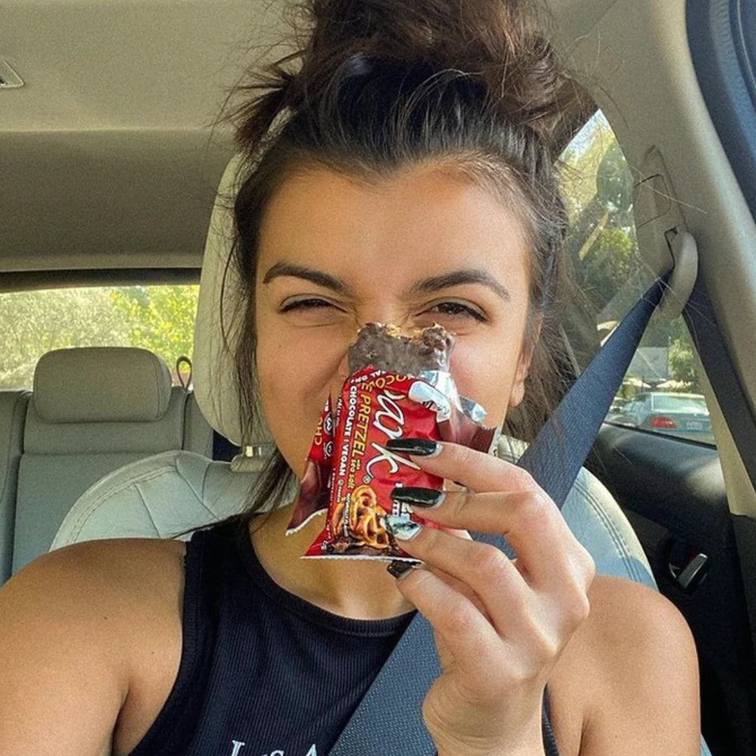 Woman in car holding a hlaf eatten NuGo Dark Chocolate Pretzel in front of face