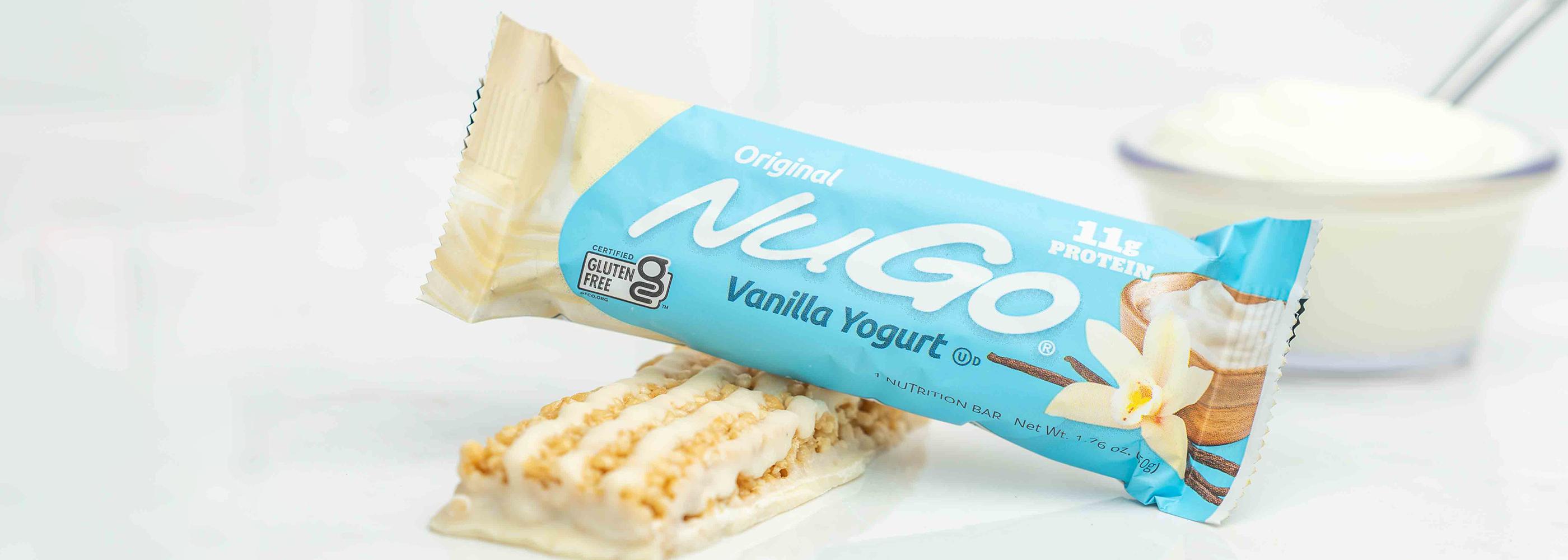 2 NuGo Vanilla Yogfurt Bars, 1 wrapped and 1 unwrapped next to a glass bowl of yogurt