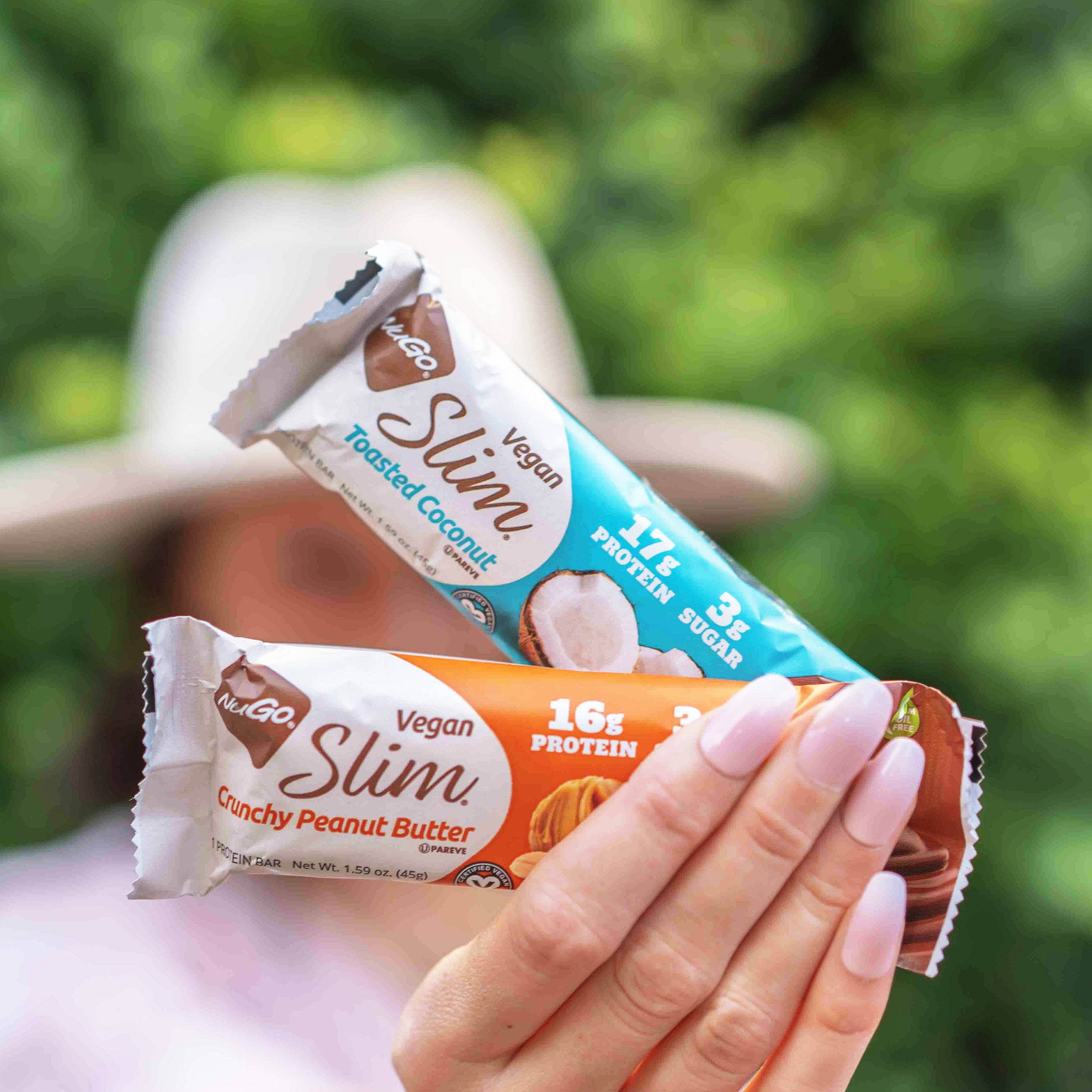 NuGo Slim Crunchy Peanut Butter and Toasted Almond in woman's hand, close up and outside